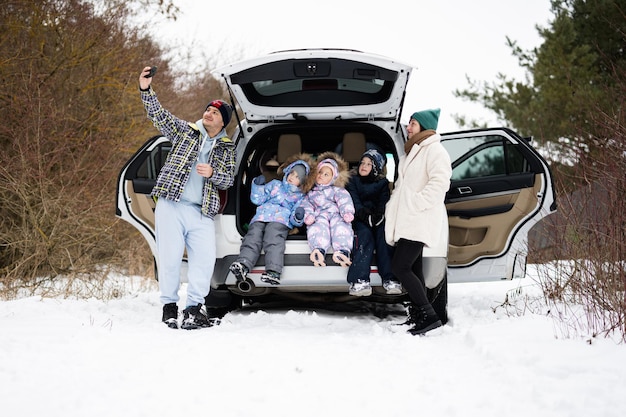 Família com filhos senta-se no carro suv com porta-malas aberto na floresta de inverno