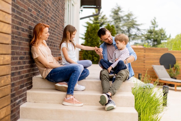 Família com mãe, pai, filho e filha sentados do lado de fora nos degraus de uma varanda frontal de uma casa de tijolos