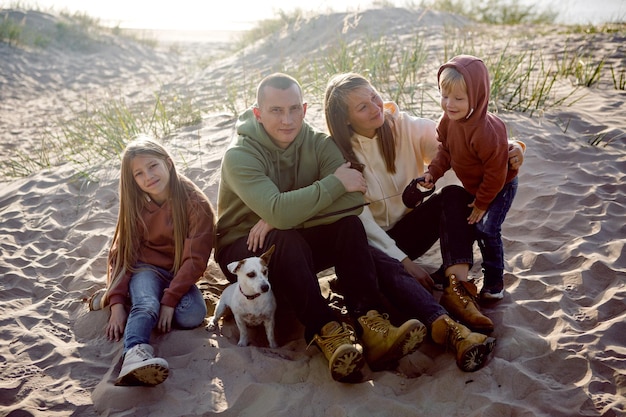 Família com um filho e uma filha e um cão sentados na areia no outono