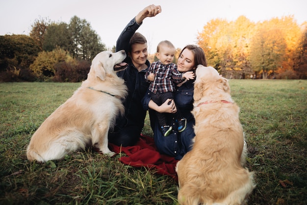 Foto família com uma criança e dois retrievers dourados em um parque de outono