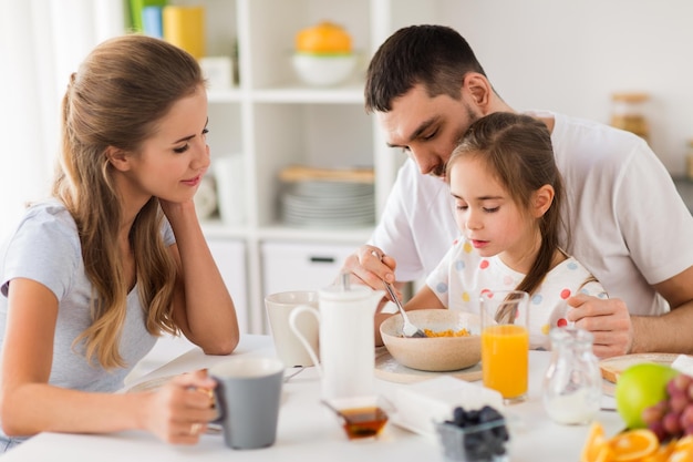 Foto família comendo e pessoas conceito mãe feliz pai e filha tomando o pequeno-almoço em casa