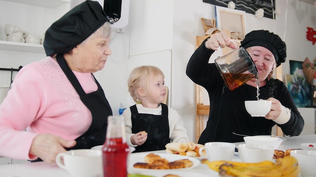 Família comendo panquecas e bebendo chá na cozinha Despejando o chá nas xícaras