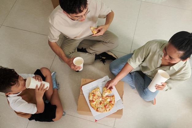 Familia comiendo pizza fresca en el piso de su nuevo apartamento vista desde arriba