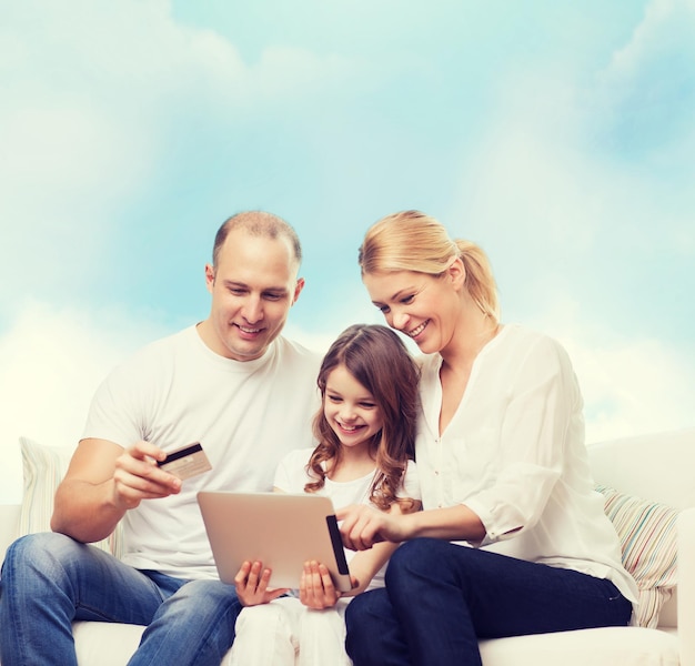 família, compras, tecnologia e pessoas - sorrindo mãe, pai e filha com computador tablet pc e cartão de crédito sobre fundo de céu azul