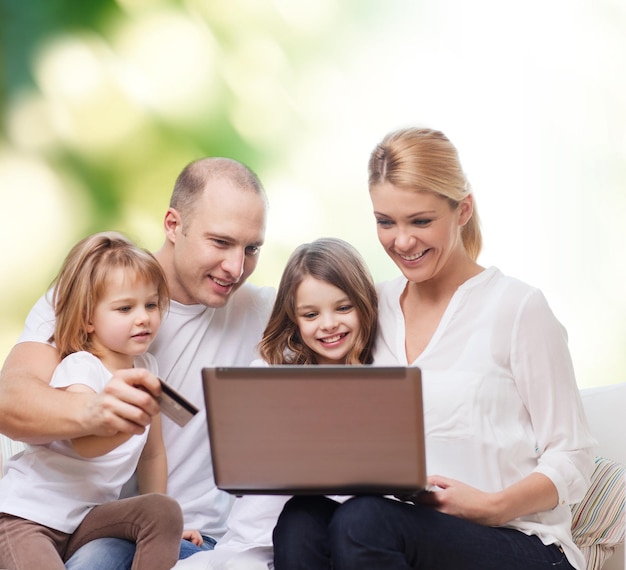 familia, compras, tecnología y gente - familia feliz con computadora portátil y tarjeta de crédito sobre fondo verde