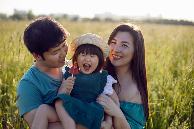 Família coreana com sua filha vai para o campo na grama ao pôr do sol