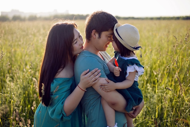 Família coreana com sua filha vai para o campo na grama ao pôr do sol