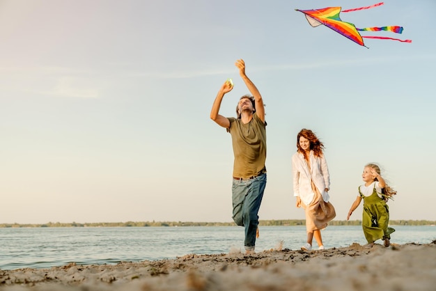 Familia corriendo por la playa dejando volar cometas padre y madre caucásicos con su hija