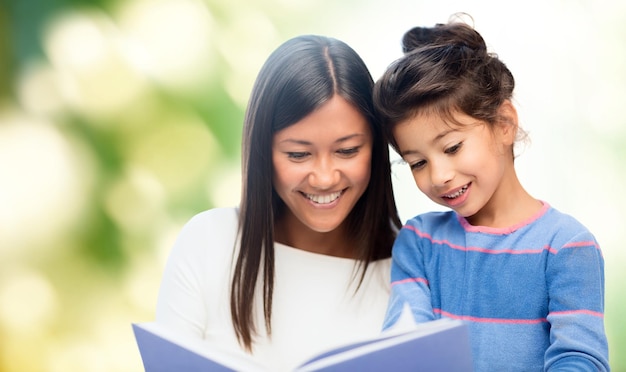 família, crianças, educação, escola e conceito de pessoas felizes - mãe e filha felizes lendo livro sobre fundo verde