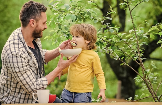 Familia y crianza feliz día del padre Niño pequeño con papá come cereal Desayuno matutino comida saludable y dieta Productos lácteos hijo y padre comiendo al aire libre A quién le importa la dieta