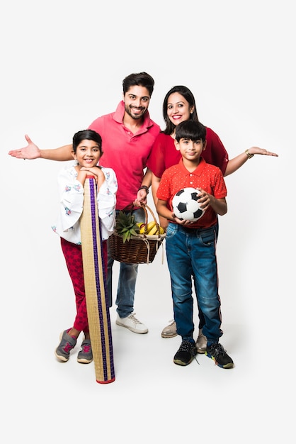 Familia de cuatro jóvenes indios que van de picnic - de pie sobre fondo blanco con canasta de frutas, tapete, fútbol y bebidas. enfoque selectivo