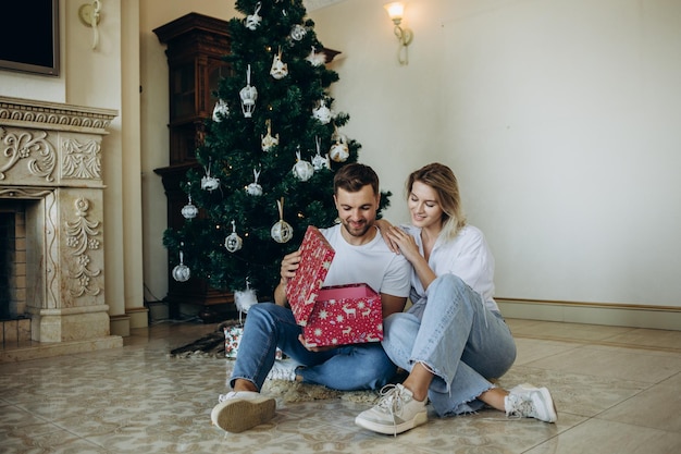 Familia de cuatro padres, mamá y papá embarazadas y dos hermanos, un niño y una niña con ropa elegante en un chalet, están listos para recibir Navidad y Año Nuevo cerca del árbol de Navidad con regalos de caja de regalo