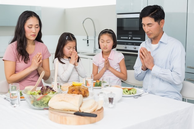 Familia de cuatro que dice gracia antes de la comida en la cocina