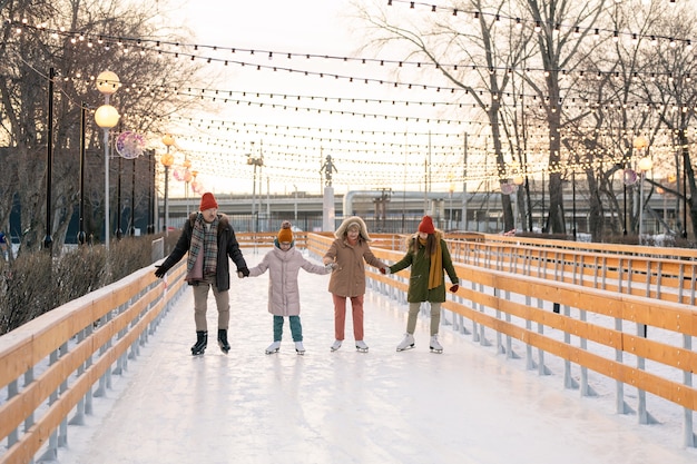 Familia de cuatro tomados de la mano y patinar juntos en la pista de hielo al aire libre durante las vacaciones de invierno