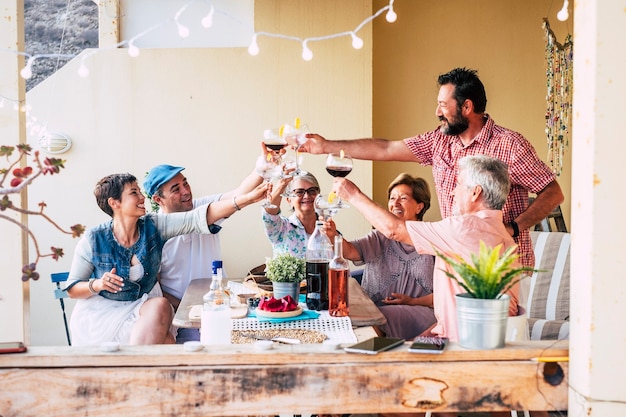 Família de amigos de grupos de idades e gerações mistas se divertem juntos tilintando e brindando durante a hora do almoço com comidas e bebidas