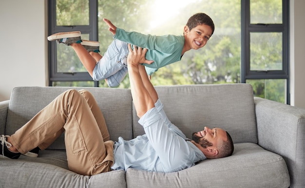 Família de crianças e amor com um homem e um menino brincando juntos em um sofá na sala de estar de sua casa Pai filho e filhos com um pai masculino se relacionando com seu filho em sua casa com um sorriso