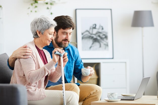 Família de dois sentados no sofá e olhando para o monitor do laptop, eles conversam online em casa