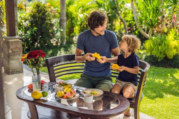 Família de dois tomando café da manhã bem servido do lado de fora de um jovem bonito servindo café e seu filho fofo comendo frutas deliciosas na hora do café da manhã