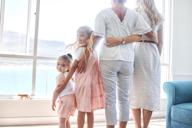 Família de garotas e janela em uma sala de estar de uma casa de férias se unindo e relaxando enquanto apreciam a vista juntos Casa de férias e crianças felizes mãe e avó e vista panorâmica na praia no verão