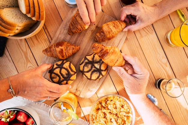 Família de grupo de amigos, vista de cima vertical, comendo croissant e comida mista para a atividade matinal de café da manhã