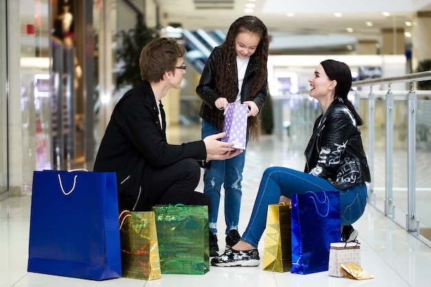 Família de jovem feliz com sacos de papel, compras no shopping. Vitrines com roupas