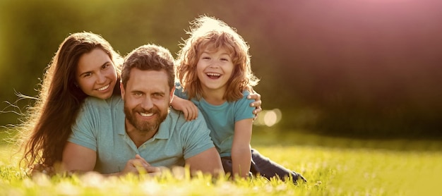 Família de mãe pai e filho criança relaxa no parque de verão Banner da família feliz Deitada na grama Jovem mãe e pai com filho criança brincam no parque descansando juntos na grama verde