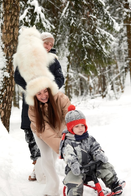 Família de mãe pai e filho se divertindo em madeira de inverno nevado com cachorro de estimação alegre