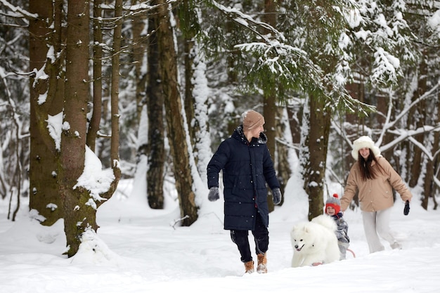 Família de mãe pai e filho se divertindo em madeira de inverno nevado com cachorro de estimação alegre