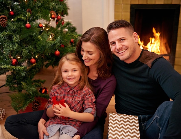 Família de Natal com menina e felicidade para celebrar a paz ou aproveitar a época festiva juntos Pais de Natal e mãe com filha pai e relaxar na sala de estar com sorriso, união e amor