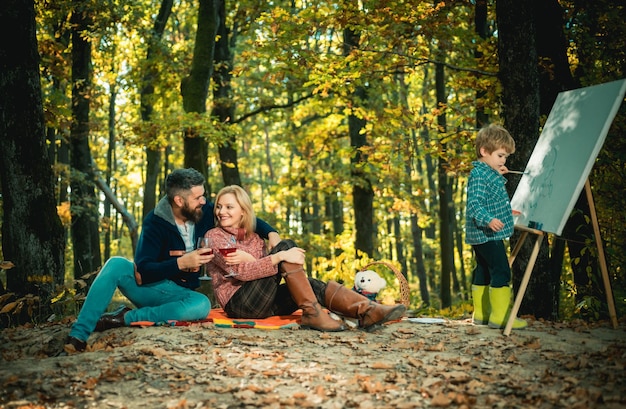 Família de outdoors de outono Família jovem desfrutando de um piquenique Pequeno filho feliz desenhando no parque Ensinando as crianças a ter boas maneiras Paixão pela arte Belo parque de outono