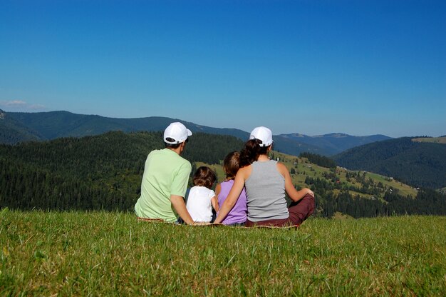 Família de pais e dois filhos sentados na grama e olhando a bela vista da montanha