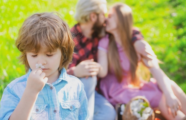 Família de primavera no piquenique ao ar livre. Pai de verão com criança no jardim ou parque. Paternidade juntos conceito de lazer. Esposa e marido se beijam.