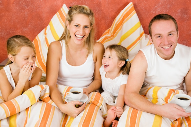 Família de quatro na cama tomando café da manhã