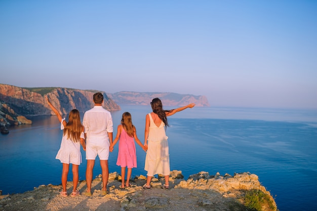 Família de quatro pessoas feliz caminhando nas montanhas ao pôr do sol