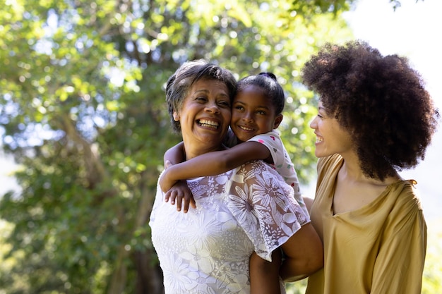 Família de raça mista de várias gerações aproveitando seu tempo em um jardim, uma mulher idosa está segurando sua neta nas costas, olhando uma para a outra e sorrindo