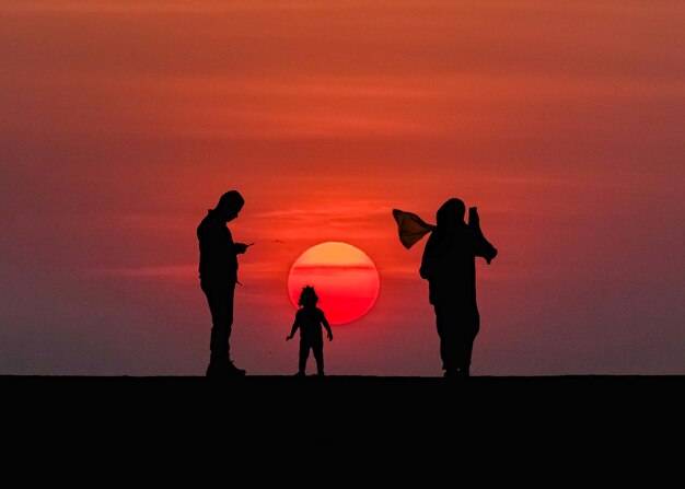 Foto família de silhueta contra o céu laranja durante o pôr do sol