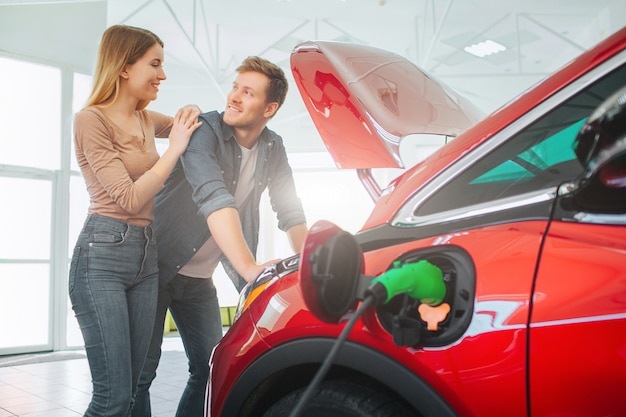 Família de sorriso nova que compra o carro elétrico na sala de exposições