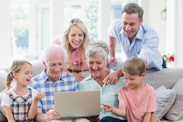 Família de várias gerações feliz usando o laptop na sala de estar