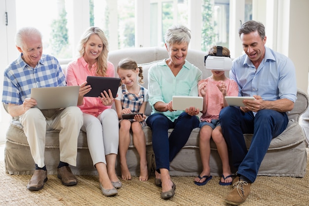 Família de várias gerações, usando tablet digital, telefone celular e fone de ouvido virtual na sala de estar