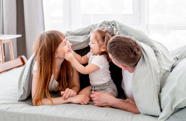 Família debaixo do cobertor na cama