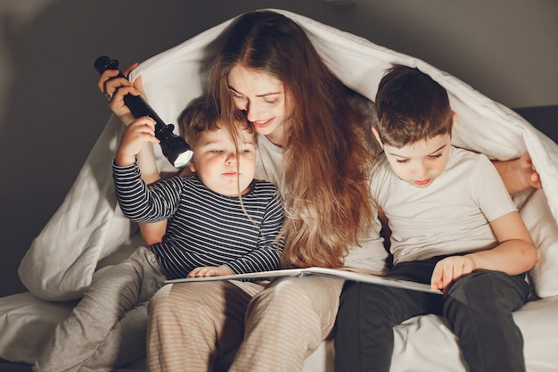 Familia debajo de la manta en la cama leyendo un libro.