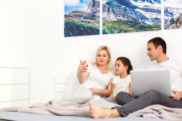 Foto família deitada na cama usando um laptop