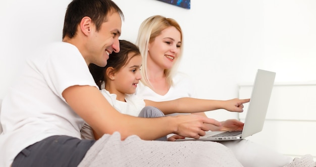 Foto família deitada na cama usando um laptop