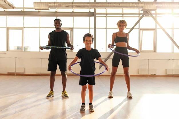 Foto familia deportiva afroamericana en uniforme deportivo gira el hula hoop y hace ejercicios en el gimnasio