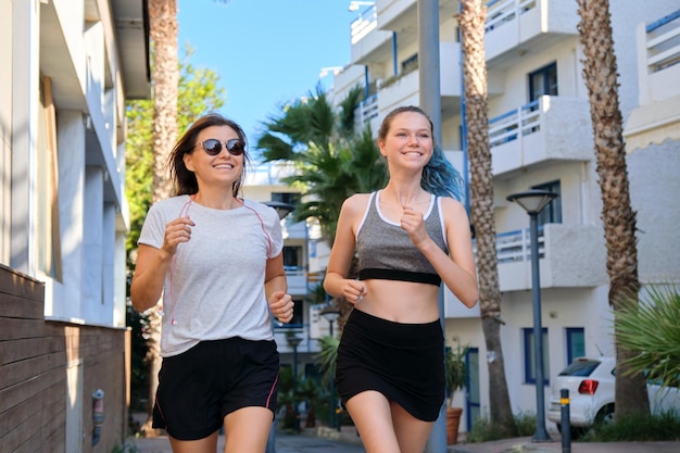 Familia deportiva amistosa activa, madre e hija adolescente corriendo juntos. Fondo de la calle de la ciudad tropical, hermosas mujeres felices para correr