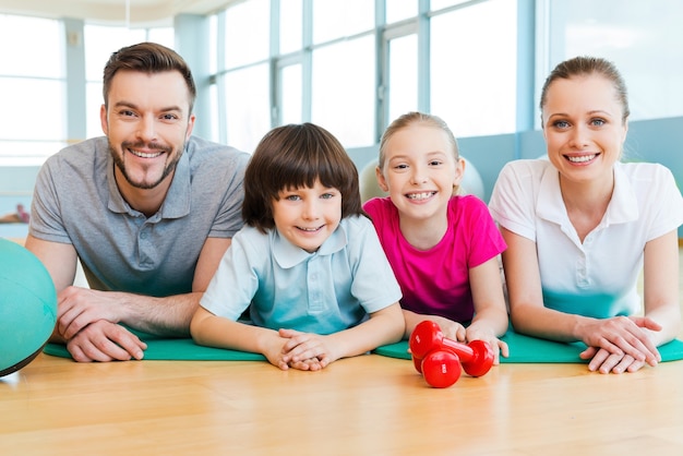 Familia deportiva. Familia deportiva feliz que se une entre sí mientras está acostado en la colchoneta de ejercicio juntos