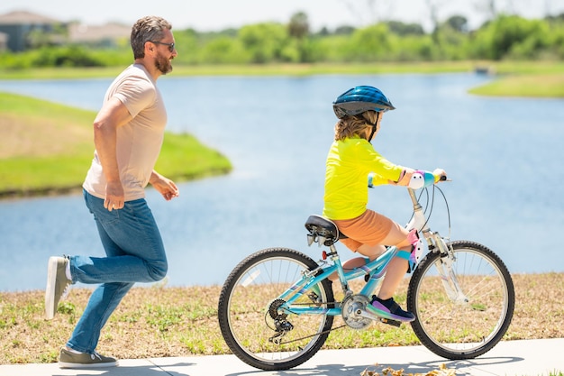 Familia deportiva padre e hijo montando bicicleta en un parque niño en casco de seguridad montando bicicleta un día de verano