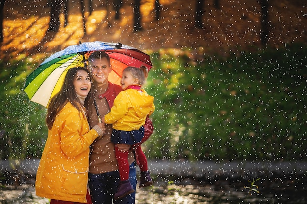Familia divertida feliz con coloridos paraguas bajo la lluvia de otoño.