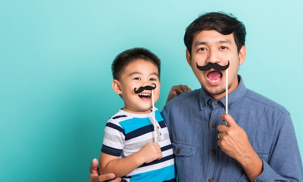 Familia divertida feliz padre inconformista y su hijo hijo con accesorios de bigote negro para la cara de cerca de la cabina de fotos