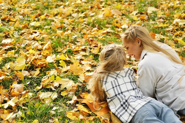 La familia se divierte en el parque La niña y la madre se acuestan en una manta de espaldas a la cámara y miran las hojas de otoño Foto horizontal